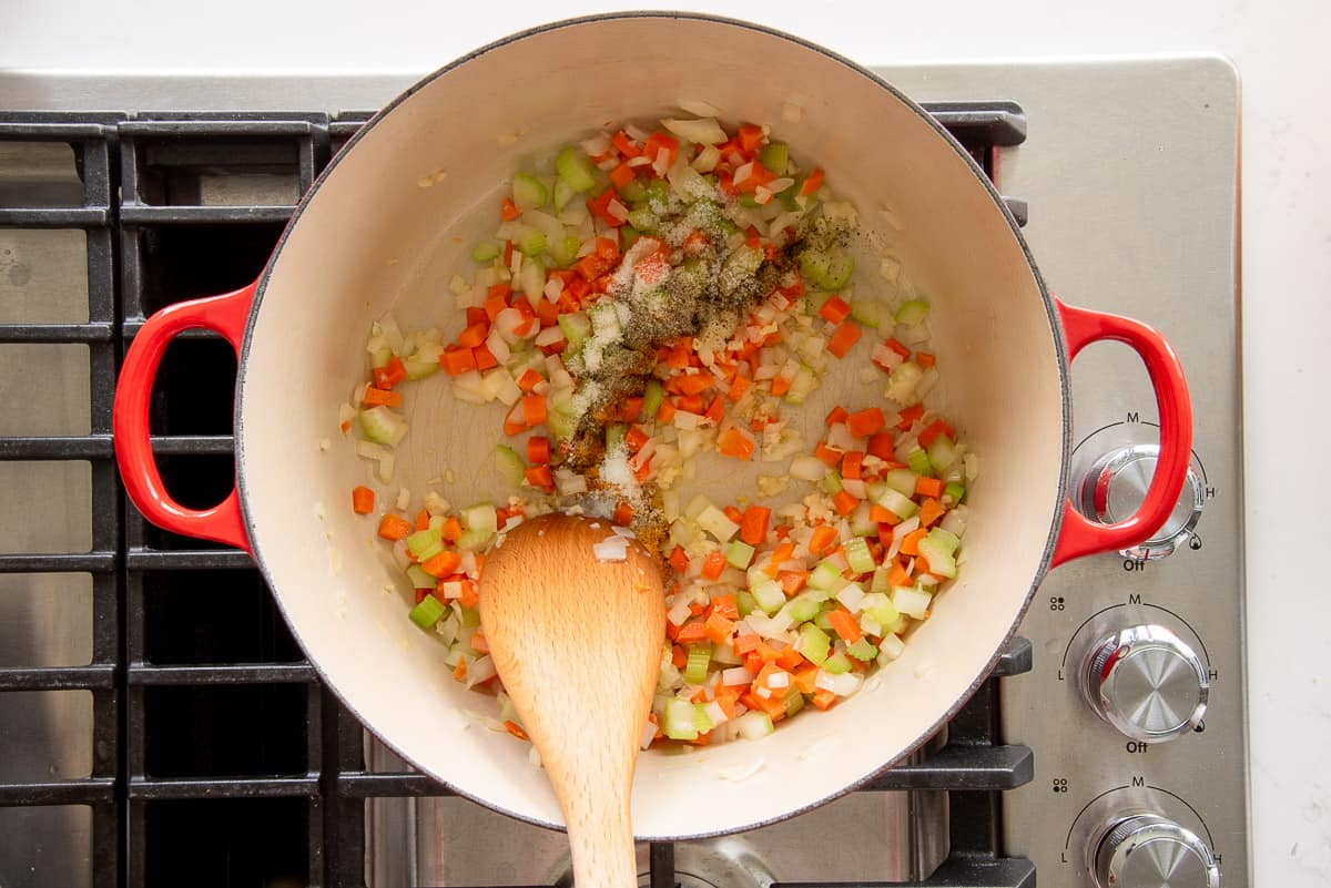 The mirepoix and spices are sautéed in a red dutch oven on the stove.