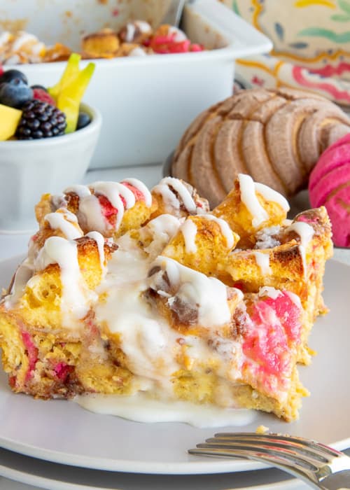 Concha Breakfast Bake on a white plate in front of a plate with multi-colored conchas and a mug of coffee.