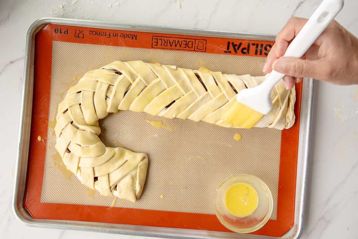 A hand uses a white pastry brush to cover the pastry in egg wash.