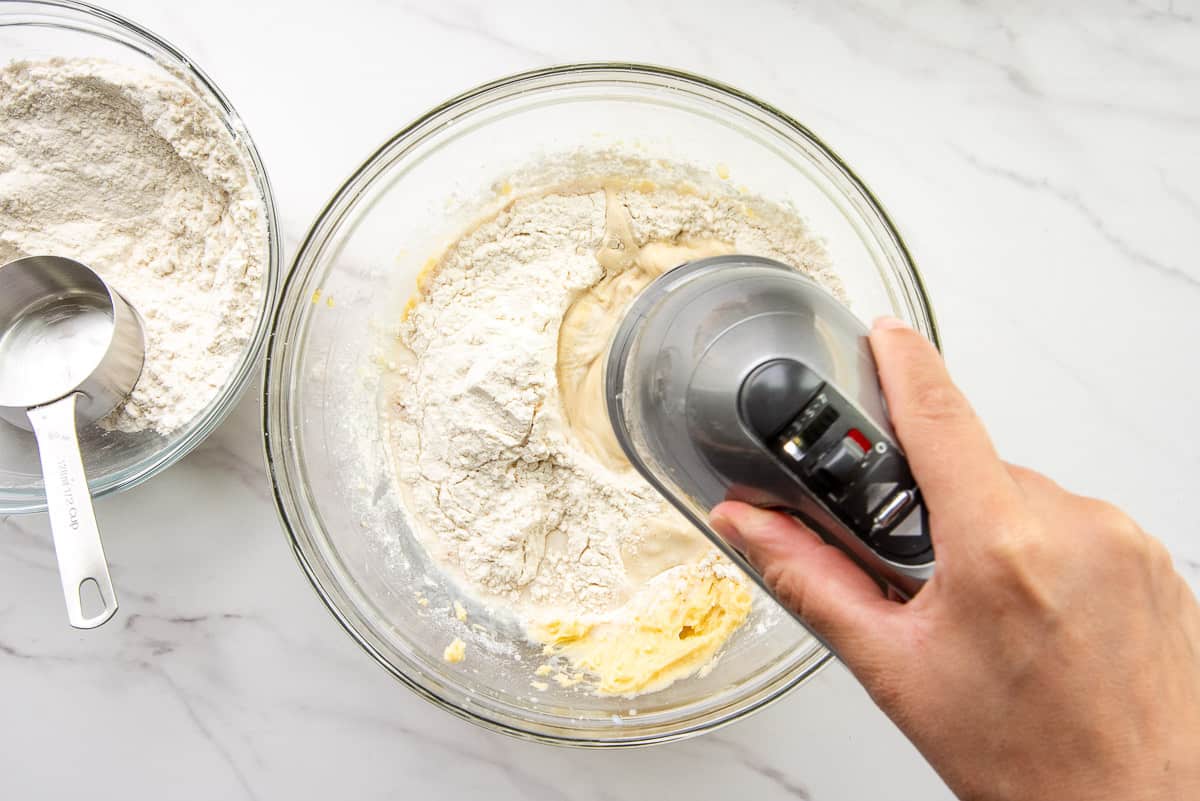 The flour is added to the ingredients in the bowl using an electric hand mixer.