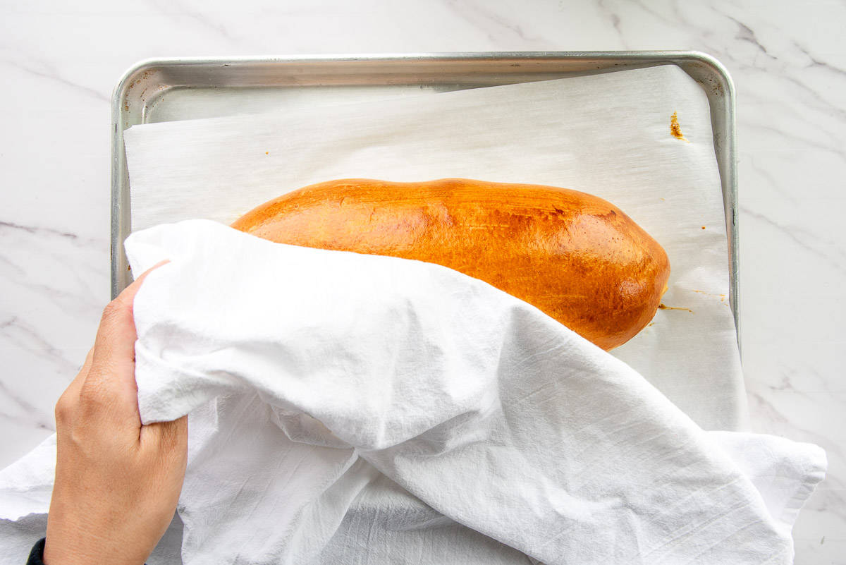 A towel is placed over the loaf immediately after it comes out of the oven to keep the crust soft.