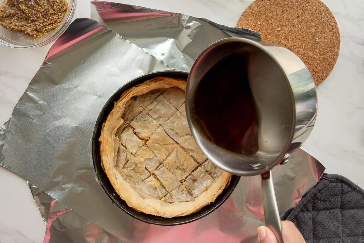 The syrup is poured over the par-baked baklava crust in a springform pan.