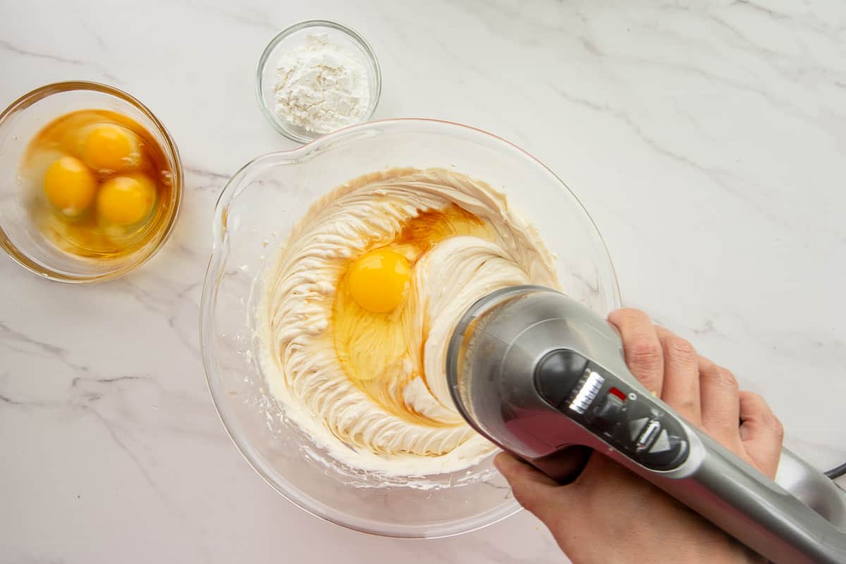 An electric hand mixer mixes the batter after eggs are added to it in a glass mixing bowl.