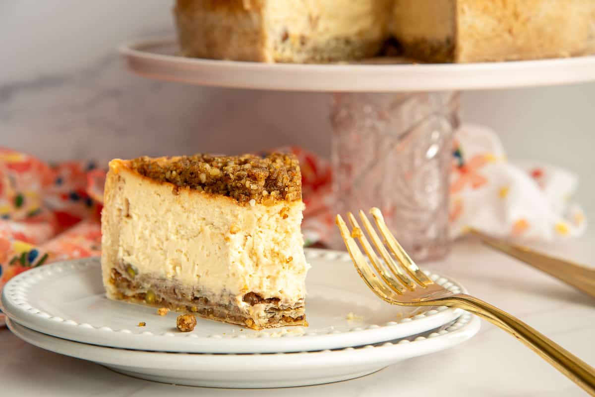 A slice of Honey Baklava Cheesecake on a white plate with a bite removed.