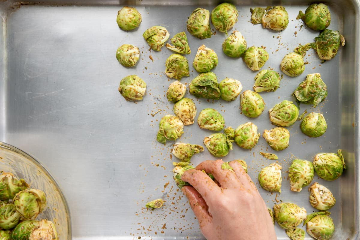 A hand lays the raw sprouts on a sheet pan cut side down.
