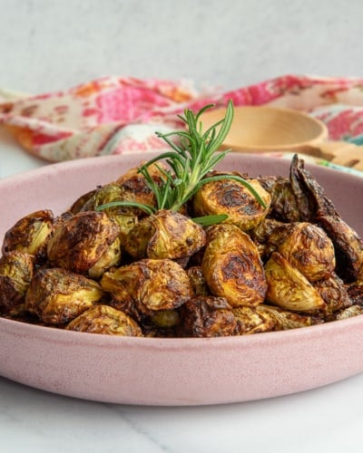 Roasted Balsamic Brussel Sprouts in a pink bowl garnished with a sprig of rosemary.