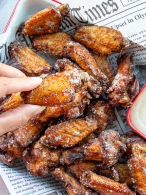 A hand holds a flapper over a tray of Salt and Vinegar Chicken Wings.