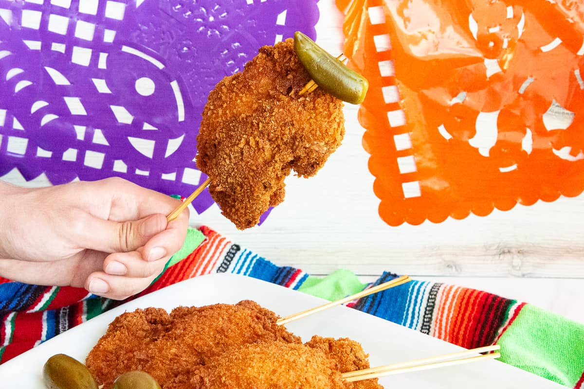Hand holding Chicken On A Stick in front of purple and orange banner.