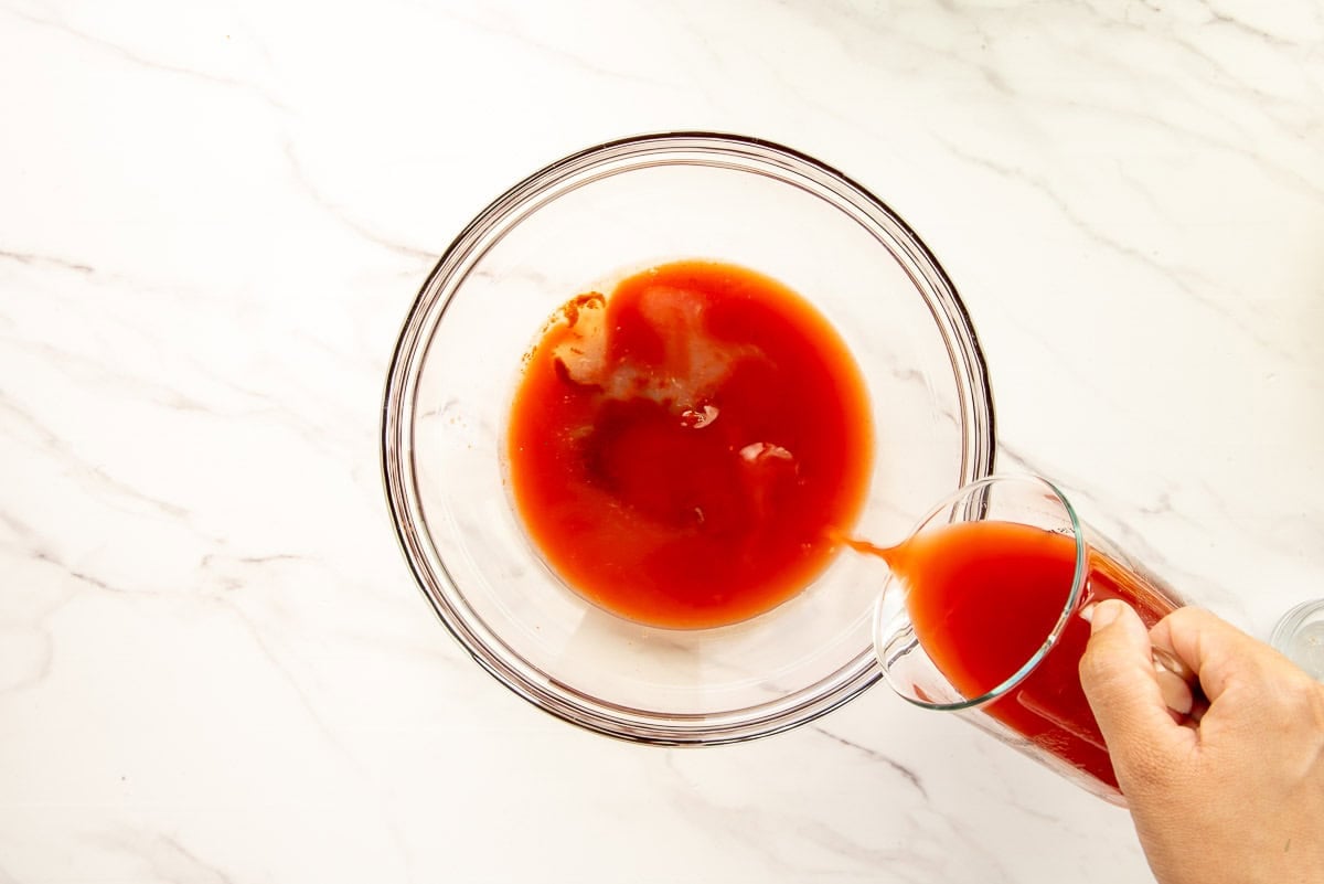 Clamato tomato juice is combined with the other liquids in the recipe in a glass mixing bowl.