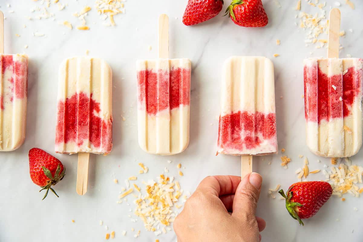 A hand grabs a Coconut Strawberry Popsicles from a line up of popsicles.