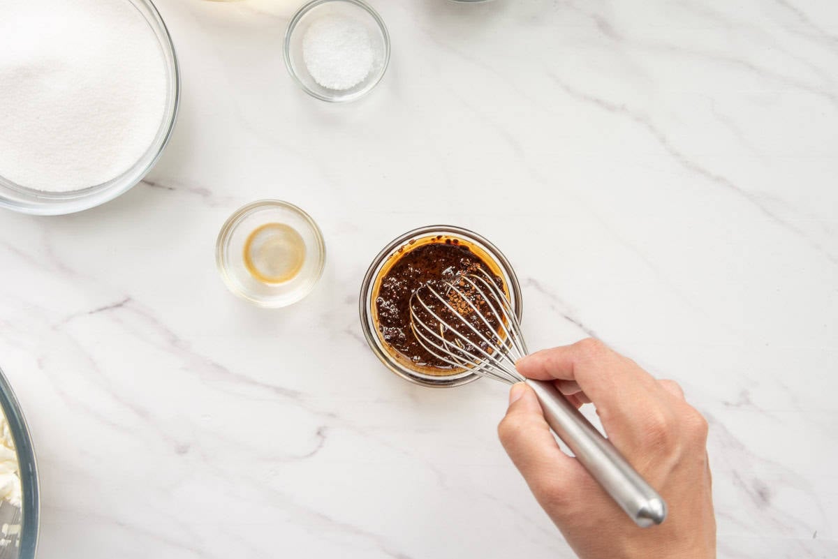 A whisk is used to dissolve instant espresso in vanilla extract and hot water.