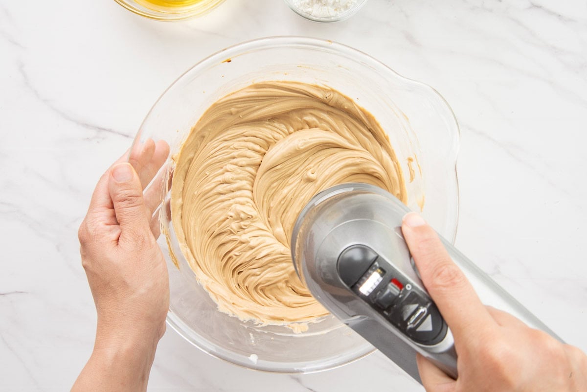 A hand mixer blends the batter together in a glass mixing bowl.