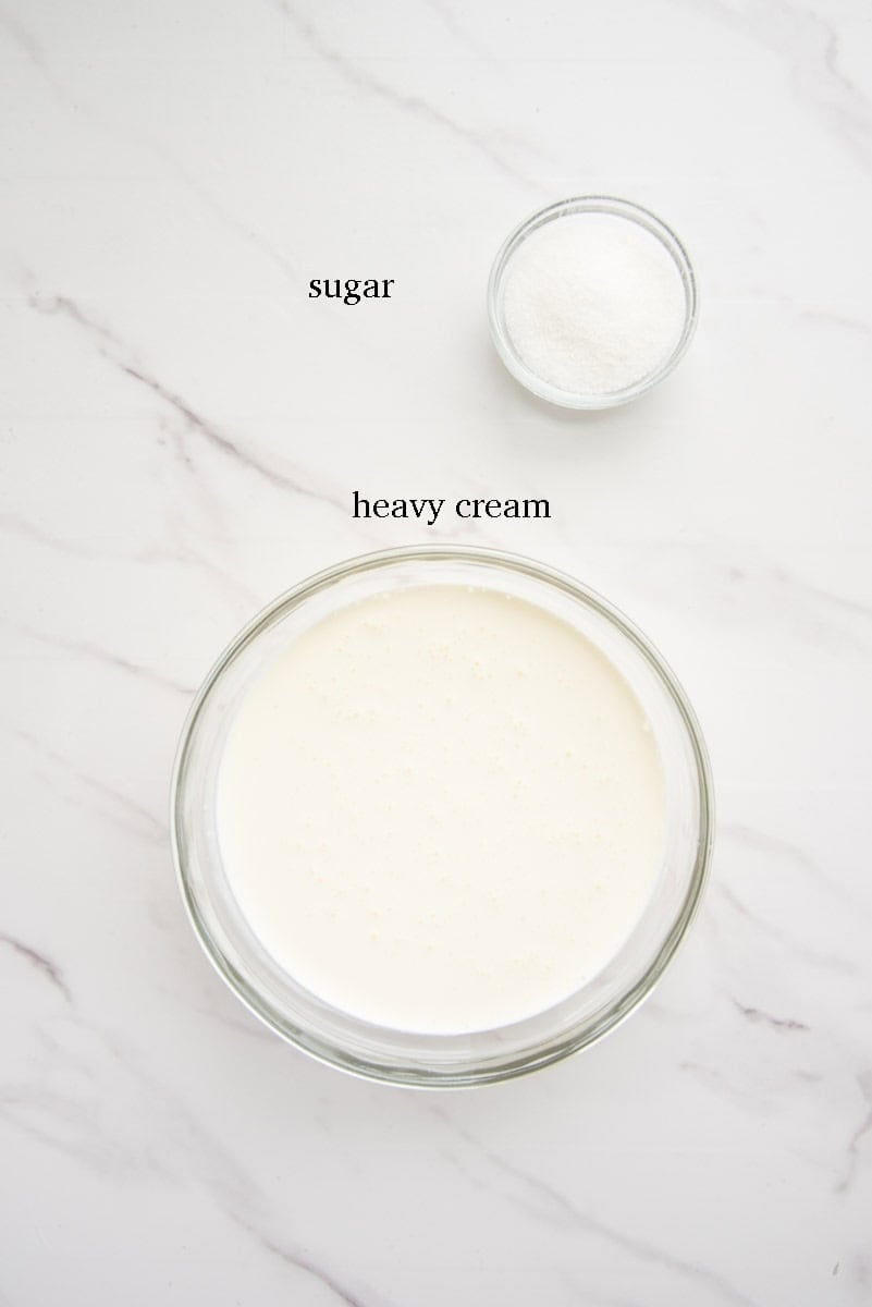 The ingredients needed to make the whipped cream are on a white countertop and labeled with black text.