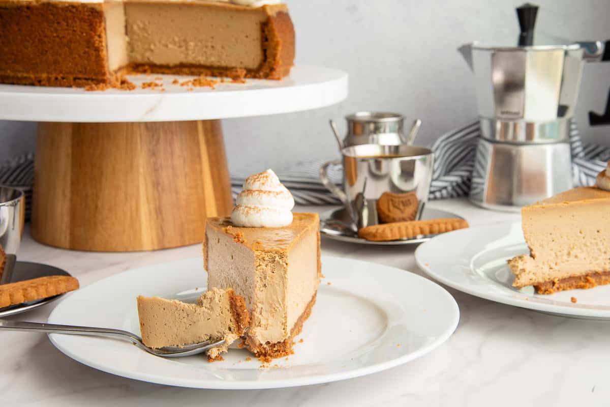 A bite of Espresso Cheesecake with Biscoff Crust lays on a fork that is propped on a dessert plate with a slice of cheesecake on it.