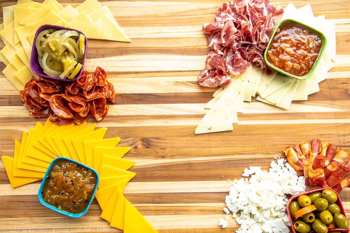 Cured meats are arranged around the bowls and cheese triangles.