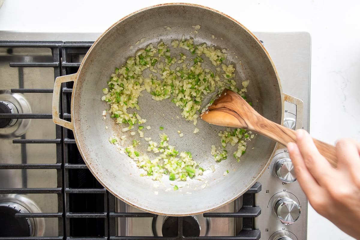 The aromatics are stirred into the oil in a pot with a wooden spoon.