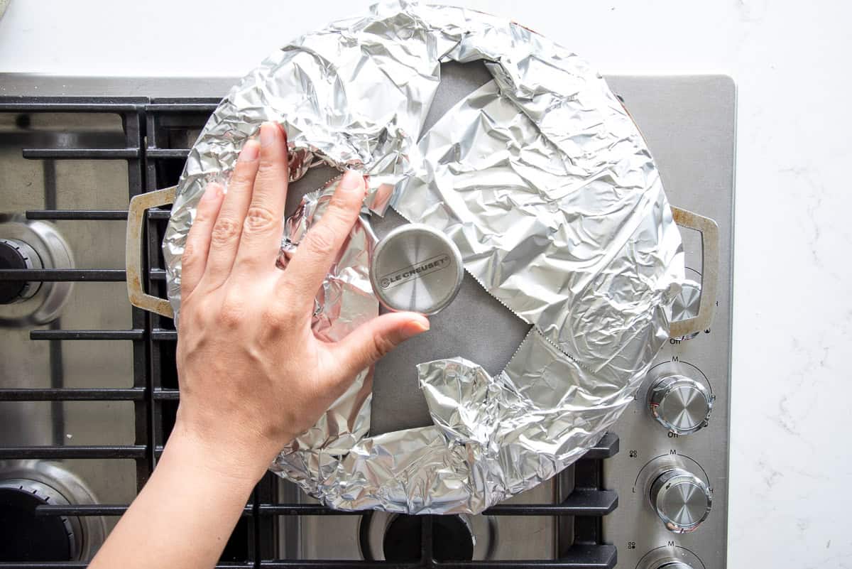 A lid is presses down a piece of aluminum foil onto the pot where the rice is cooking.