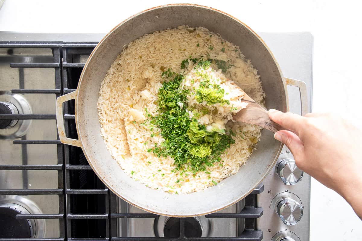 A spoon is used to fold the lime zest and chopped cilantro into the cooked rice.