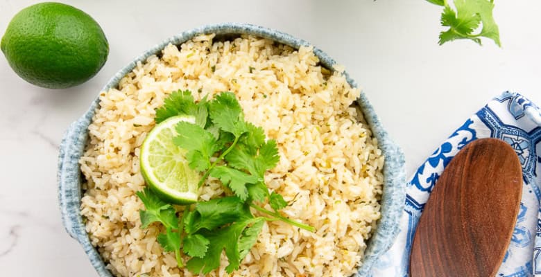 A blue and white speckled bowl of Spicy Cilantro Lime Rice garnished with a lime wedge and cilantro leaves.