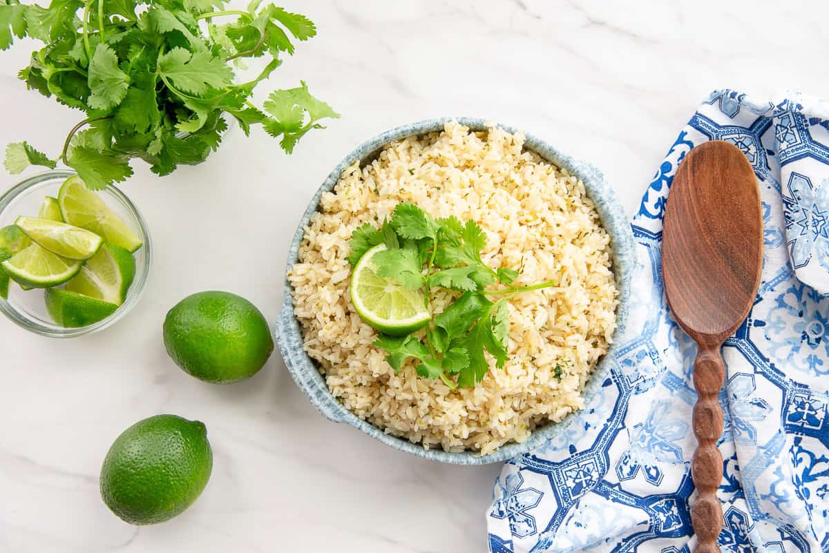 Spicy Cilantro Lime Rice in a serving bowl next to a dark wooden spoon, limes, and fresh cilantro.