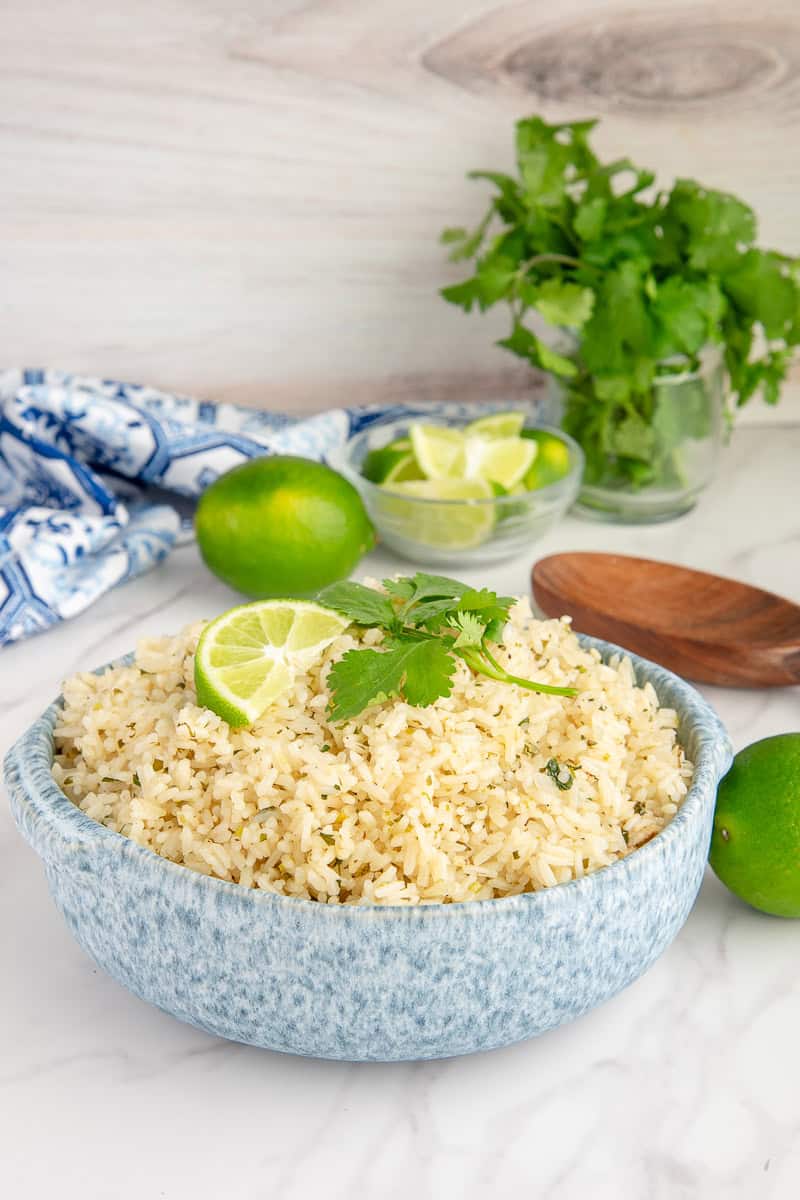 A bowl filled with Spicy Cilantro Lime Rice and garnished with a wedge of lime and a sprig of cilantro.