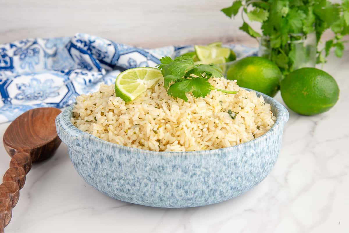 Spicy Cilantro Lime Rice in a blue and white bowl with limes and cilantro in the background.