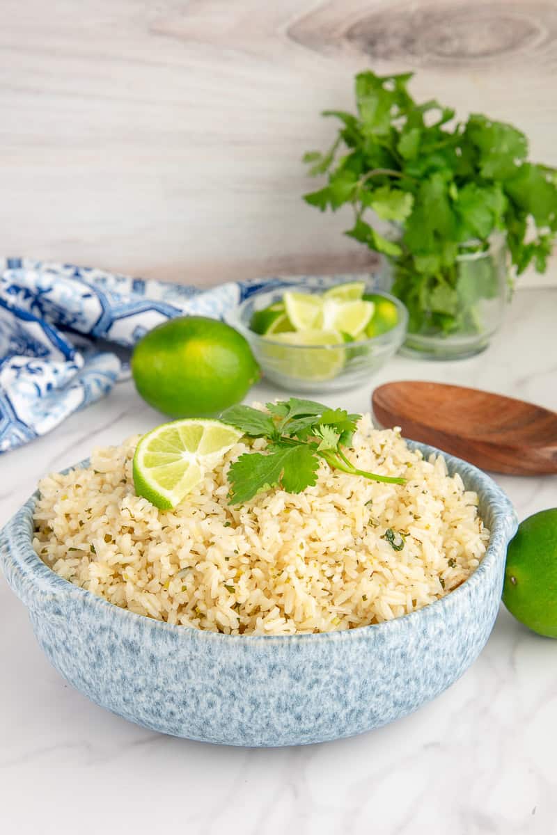 A blue and white speckled bowl full of Spicy Cilantro Lime Rice and garnished with lime and cilantro leaves.