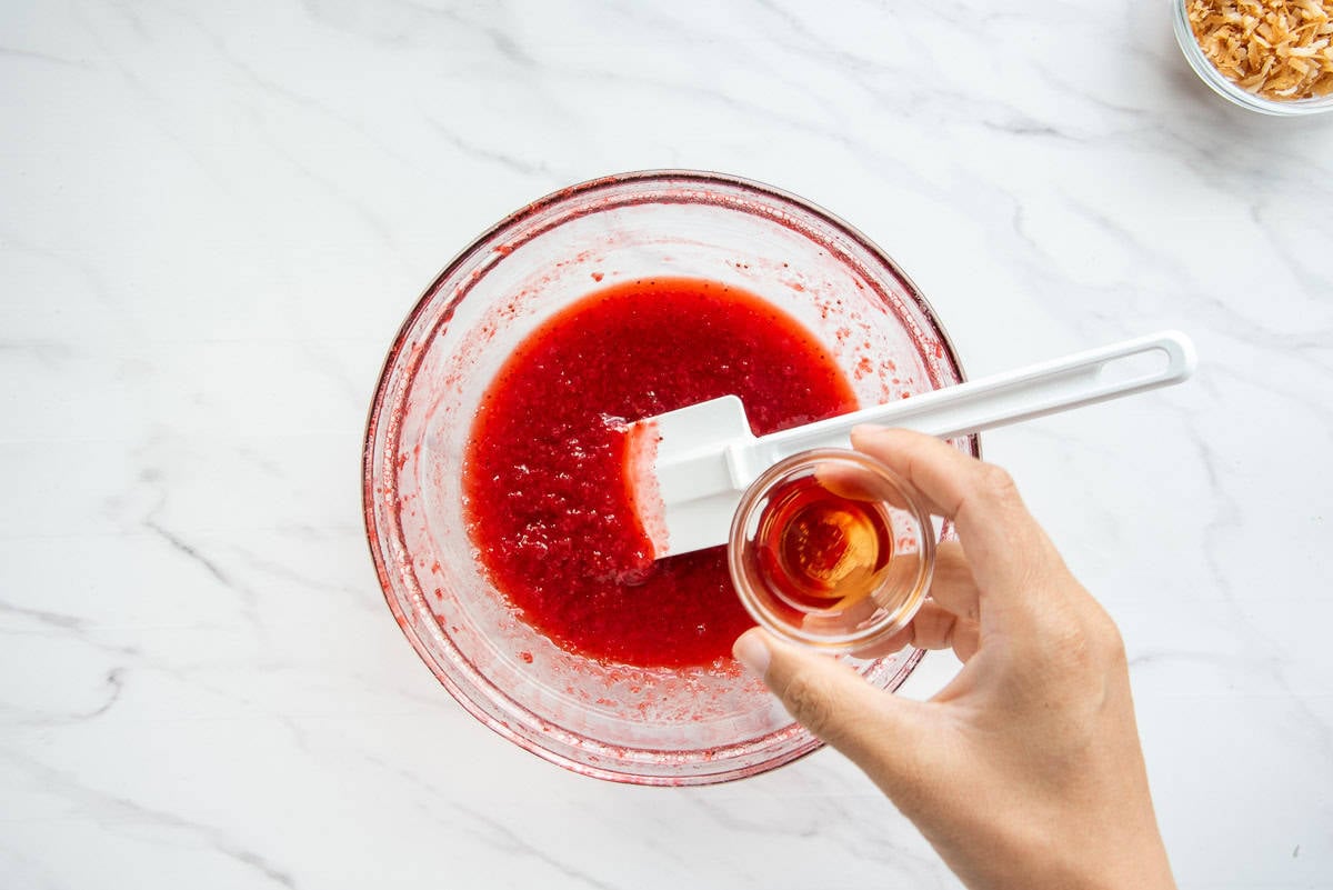 Strawberry extract is poured into the pureed berry mixture in a small bowl.