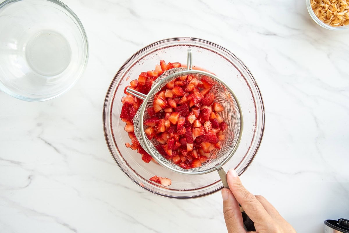 A portion of the fruit is strained over a bowl with the rest of the fruit.