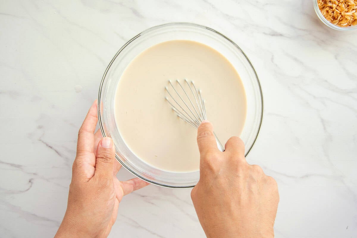 The two milks are being whisked together in a glass mixing bowl.