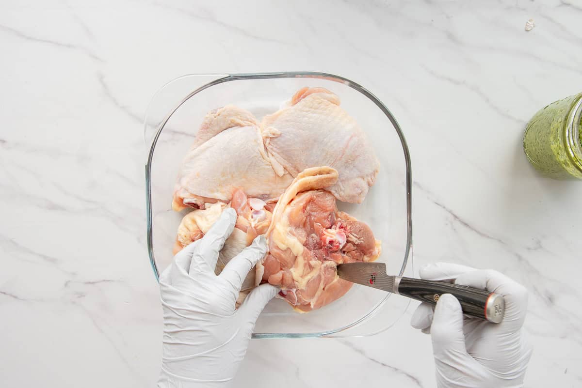 Hands use the tip of a knife to make slits in the bottom of the chicken thighs.