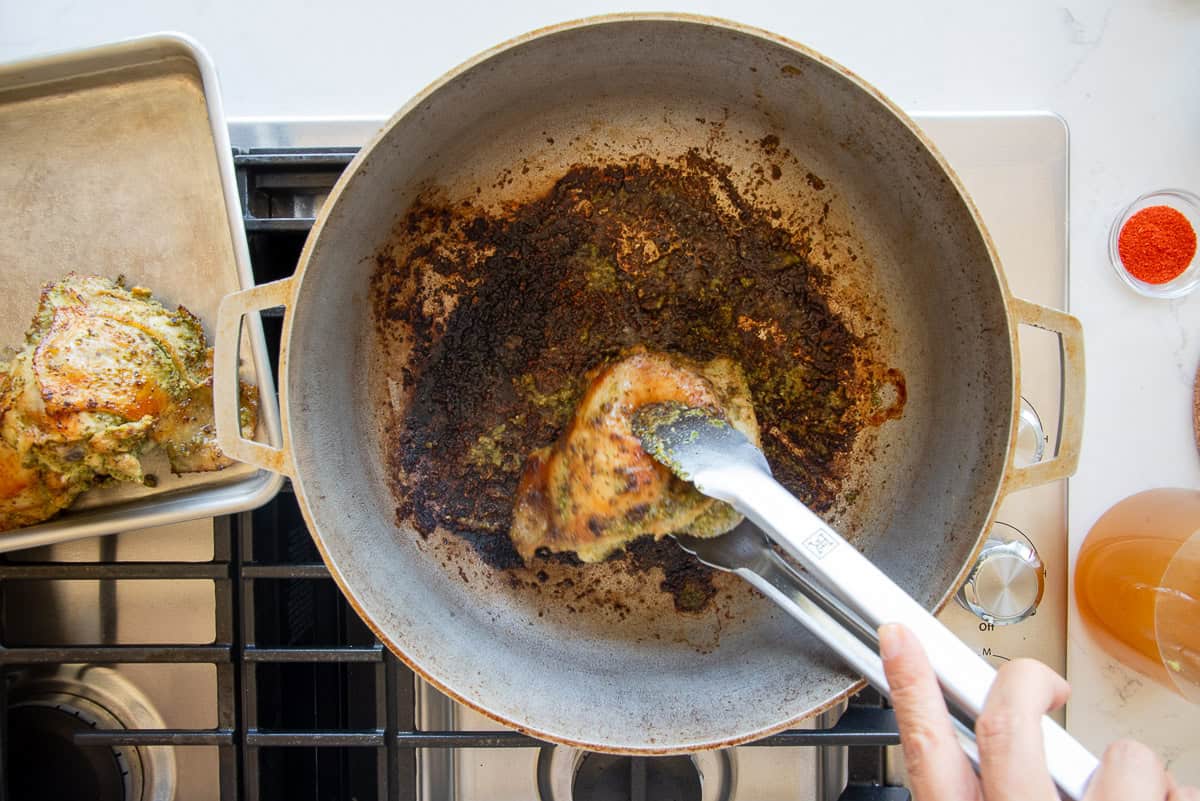 A final chicken thigh is removed from the caldero after being seared.