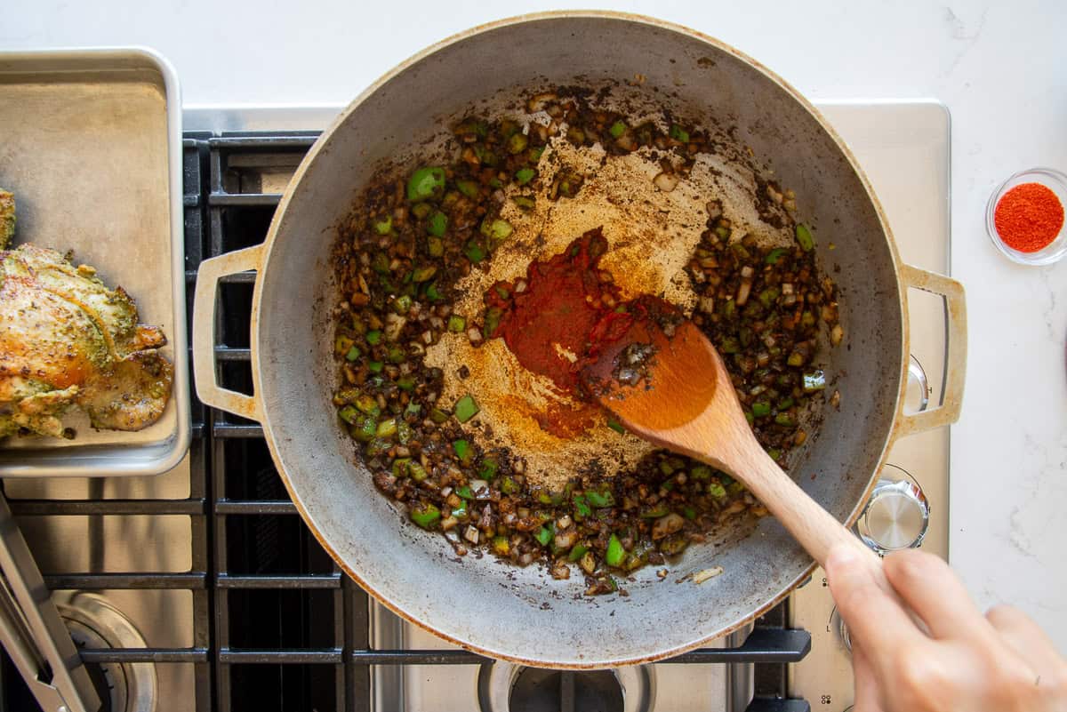 A hand uses the back of a spoon to spread the tomato paste on the bottom of the caldero to cook it.