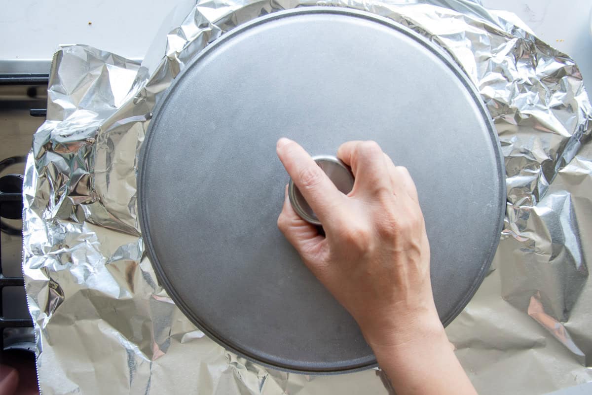 A hand placing the lid of the caldero over a piece of aluminum foil to seal the steam inside the caldero.