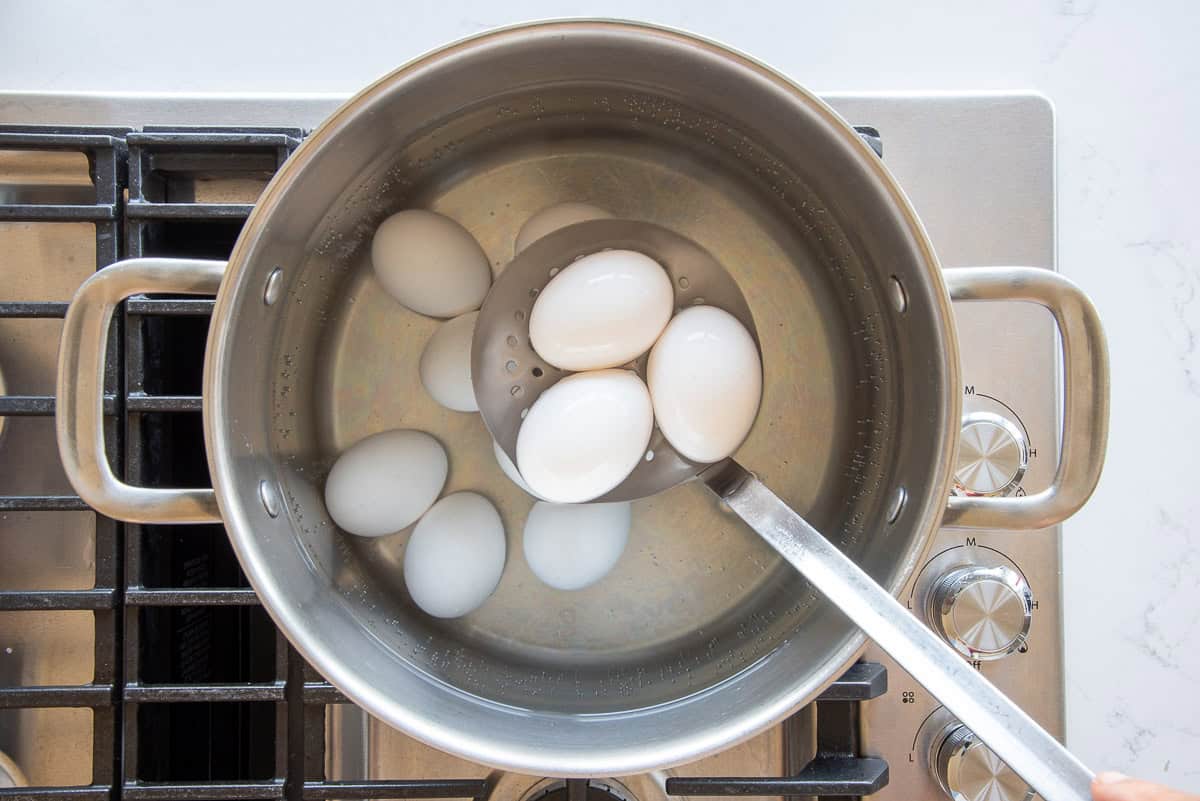 White eggs are lowered into a silver pot of simmering water with a spider.