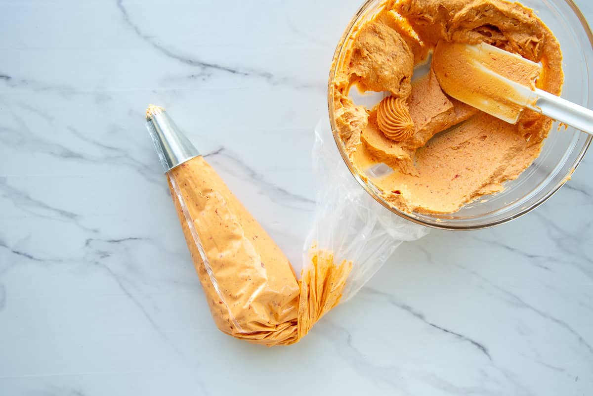 The filling is added to a piping bag which sits to the left of the bowl of filling.