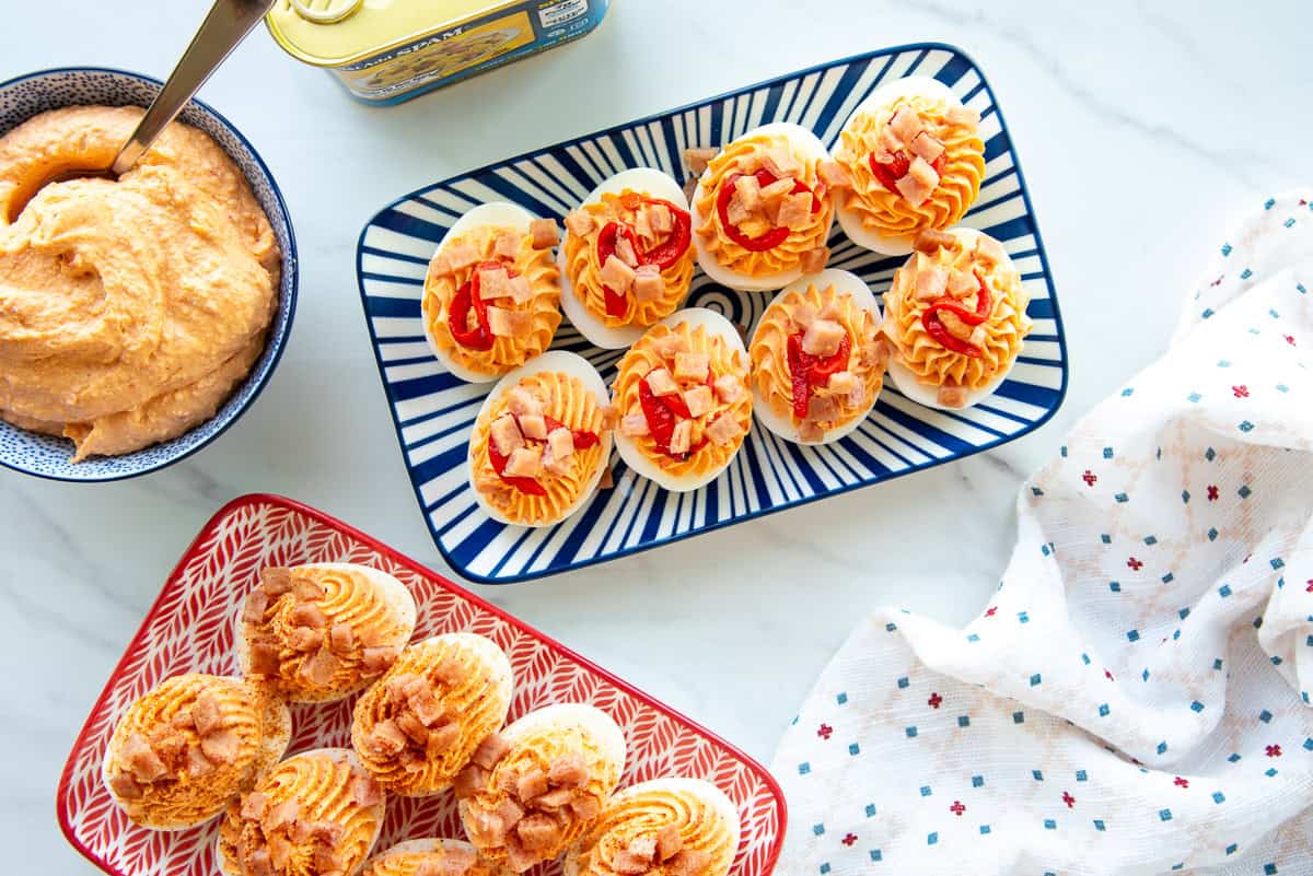 Blue and white and a red an white serving tray are topped with Mezcla Deviled Eggs and sit next to a blue and white bowl filled with the mezcla.