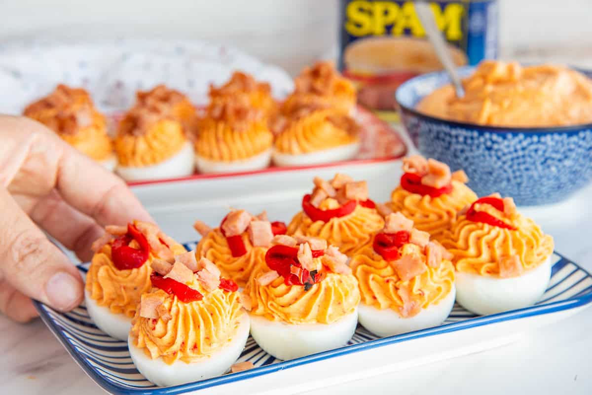 A hand picks up a Mezcla Deviled Egg from a blue and white striped platter.