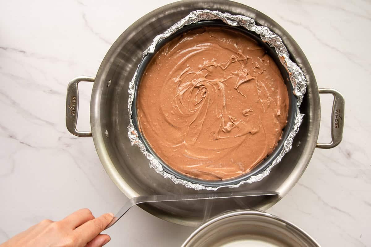 Boiling water is poured into a pan that's holding the cheesecake pan.