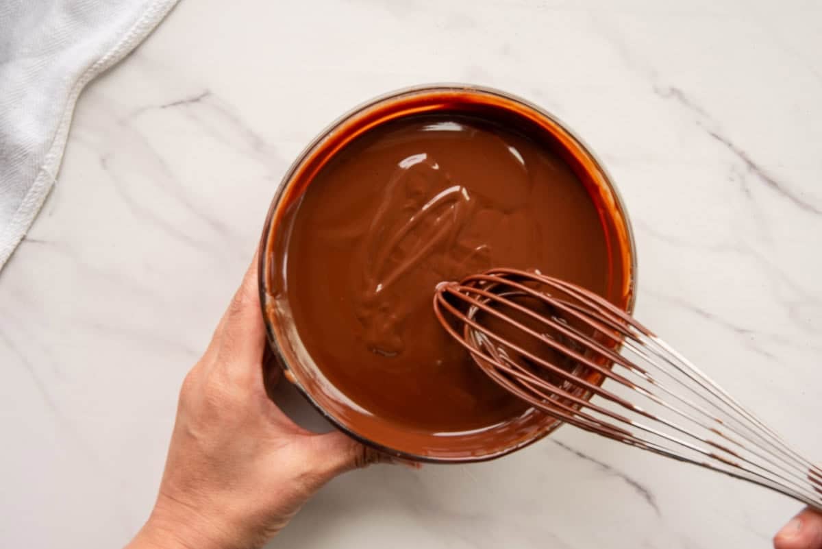 A whisk is pulled from the bowl of chocolate ganache.