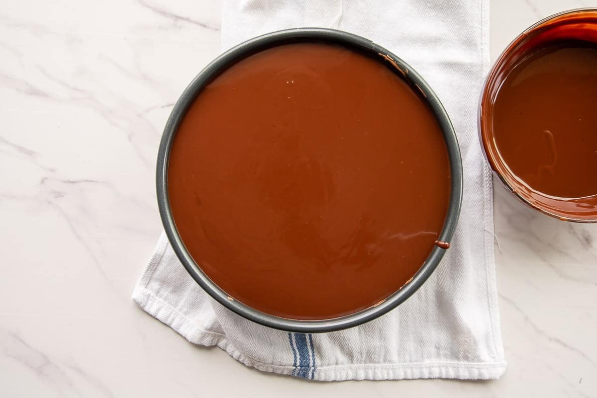 The chocolate ganache is poured onto the baked cheesecake.