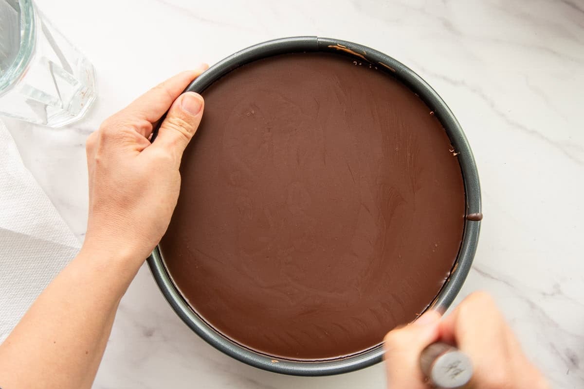 Using a paring knife to separate the chocolate ganache and cheesecake from the springform pan.