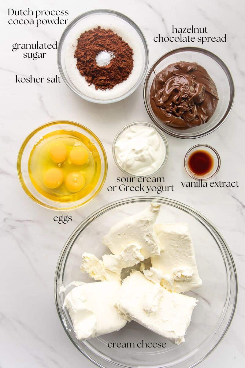 The ingredients needed to make the Hazelnut Chocolate Cheesecake are labeled on a countertop.