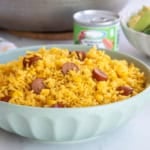 A green bowl filled with Arroz con Salchichas y Maiz in front of a tin of Vienna sausages and a bowl filled with salad.
