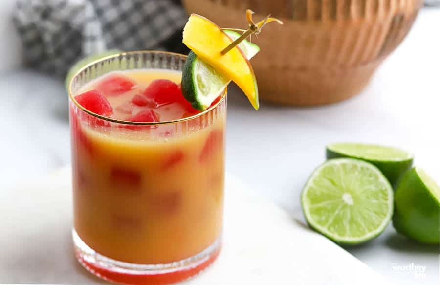 Coocnut Mango Sour garnished with fresh fruit next to cut limes.