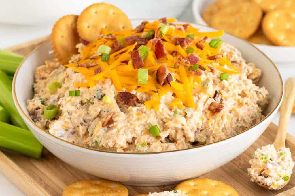 Million Dollar Dip in a white bowl garnished with crackers, cheese, and chopped bacon