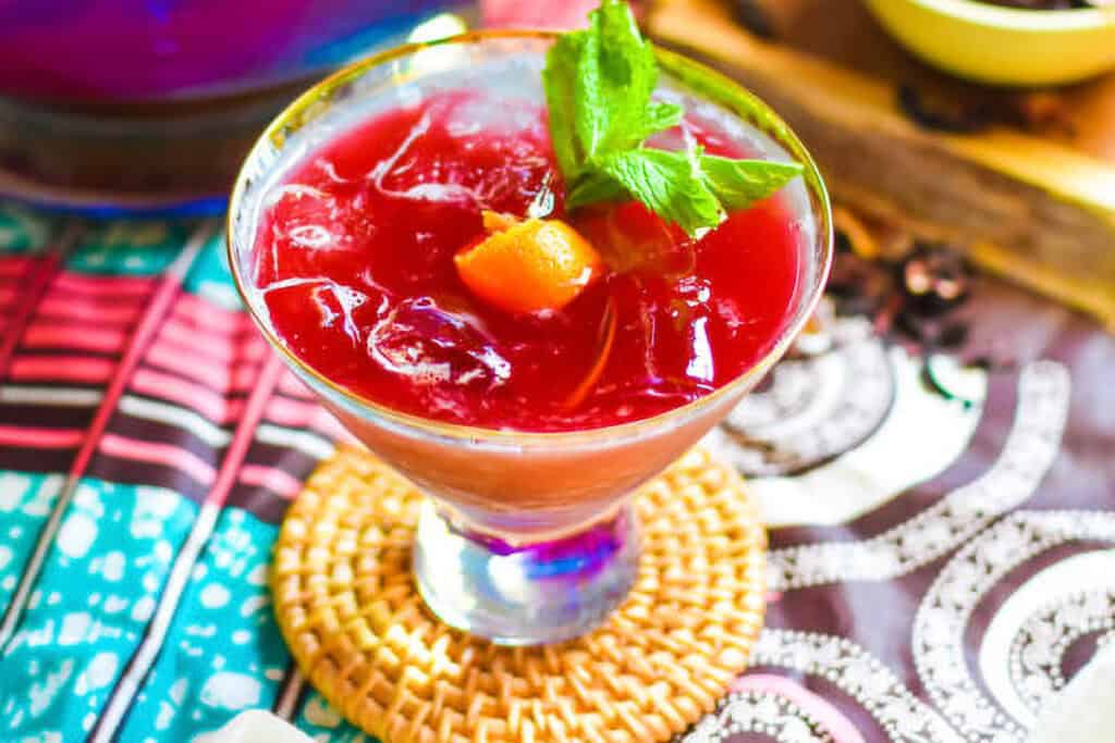 A glass of Tropical Hibiscus Sour garnished with a mint sprig and orange curl.