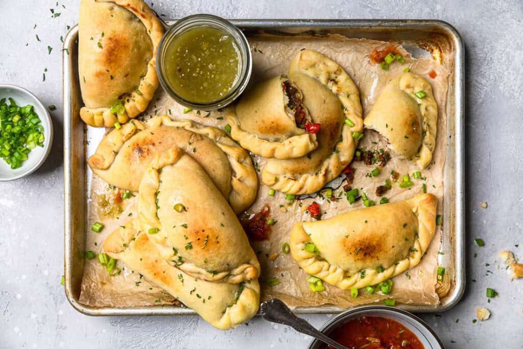 Vegan Empanadas on a sheetpan with salsa nearby.