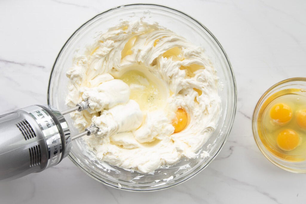 The eggs are added to the mixing bowl with the blended cheese mixture.