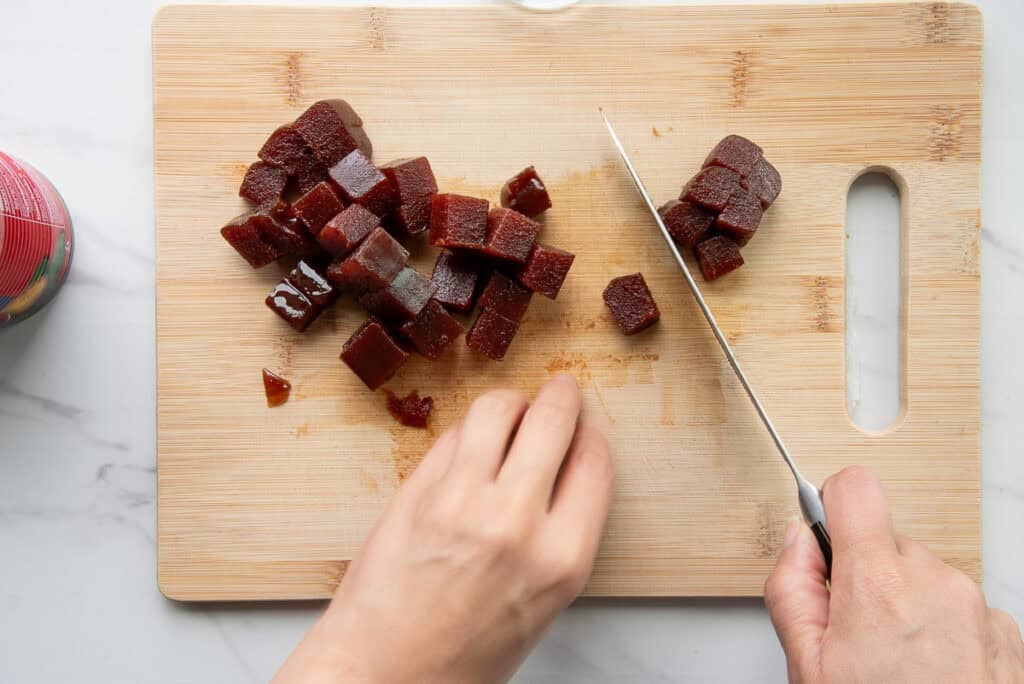 Guava paste is diced on a wooden cutting board.